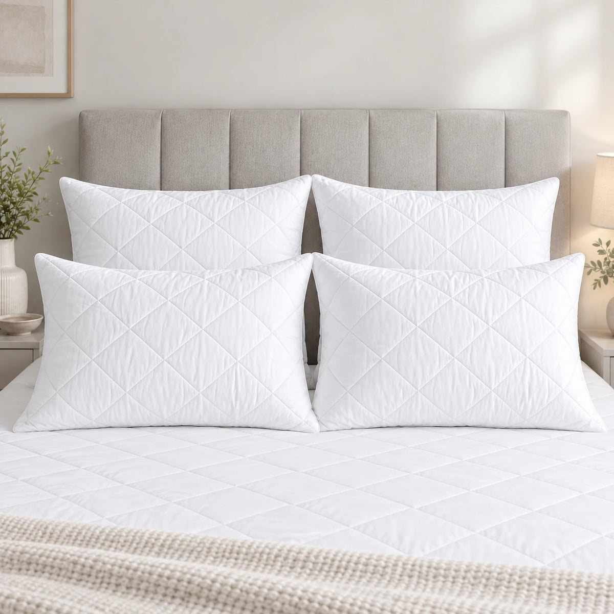 Four white quilted hollowfibre pillows with diamond-stitched covers styled on a bed